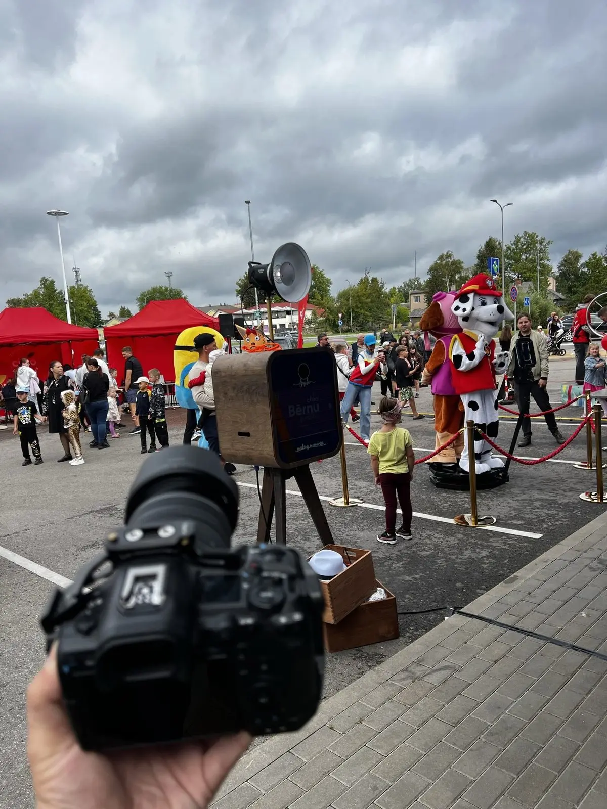 Koka foto kaste ar rekvizītiem bērnu svētkos laukumā, fonā tēli un sarkanas teltis