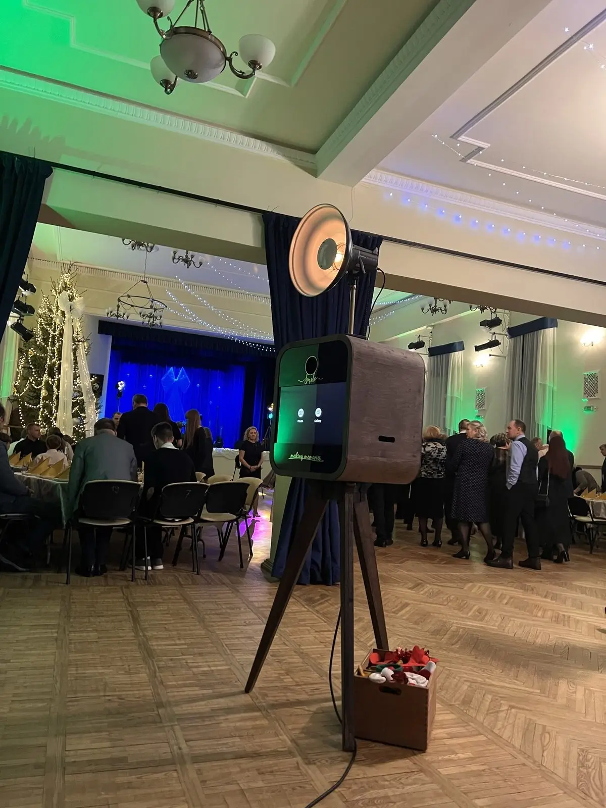 Foto kaste zaļās gaismās banketu zālē ar Ziemassvētku egli un skatuvi