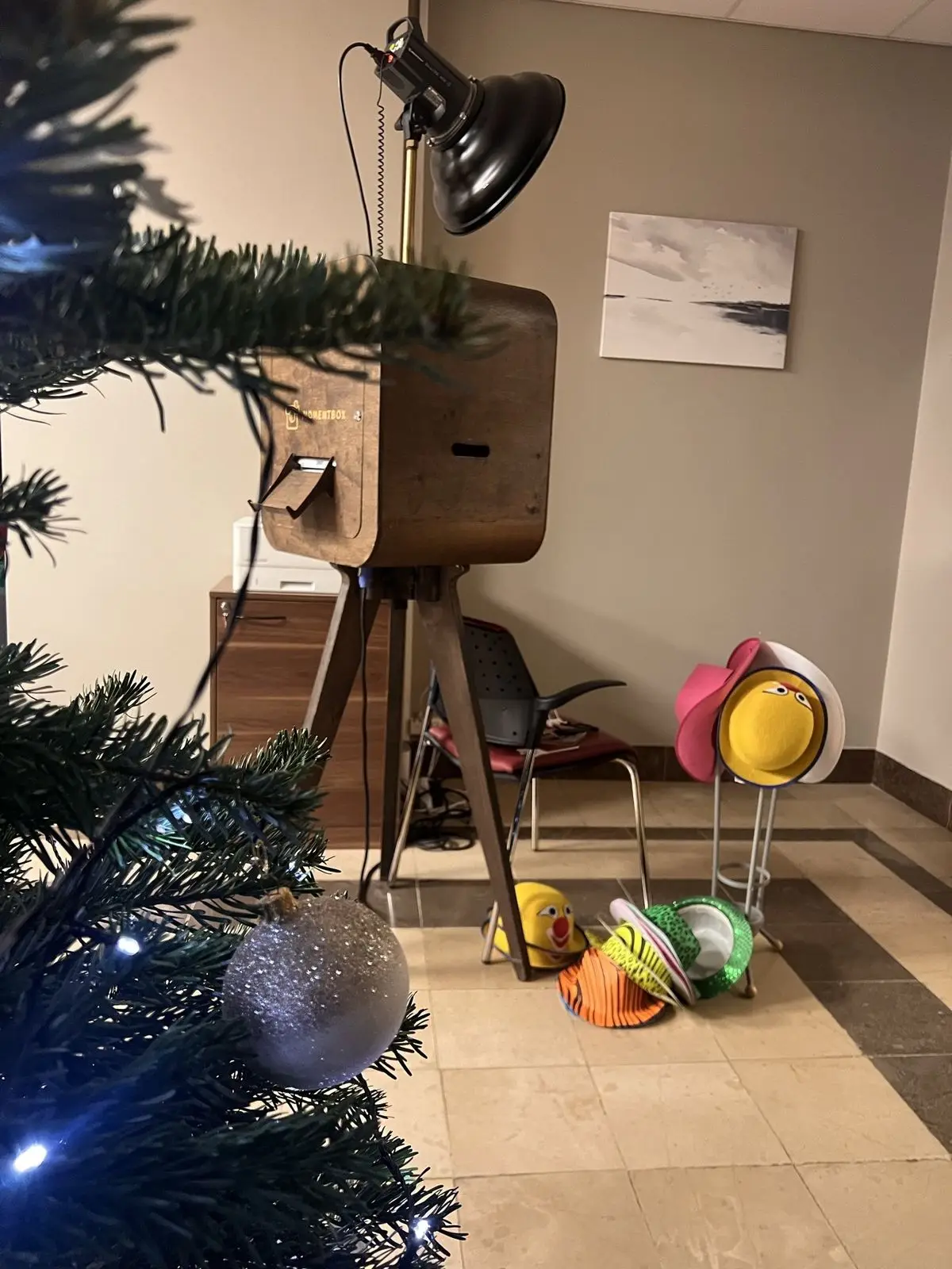 Foto kaste ar cepurēm un rekvizītiem blakus Ziemassvētku eglei